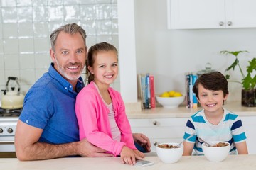 Obraz na płótnie Canvas Smiling father and kids having breakfast in kitchen