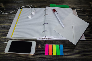 Workplace organisation: blank notepad with colorful stickers, pen and smartphone on hard wood table.