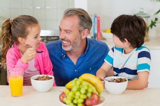 Smiling Father And Kids Having Breakfast In Kitchen