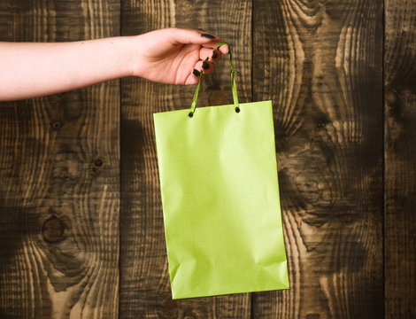 green shopping bag in female hand on wooden background