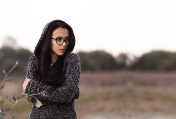 Lonely alone beautiful girl in warm sweater with hood looking aside in autumn field background....