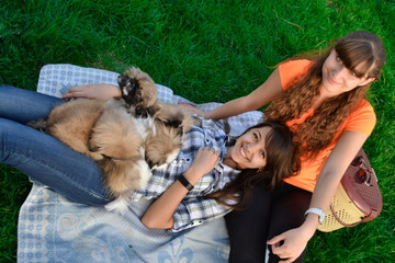 Outdoor portrait of two cute girls hugging with ginger cat and puppy of Chinese Shar Pei dog on green grass. Ywo happy smiling cheerful girl play with small fluffy Pekinese puppy outdoors in dog park