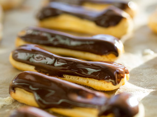 Freshly baked crispy oblong and round pastry chocolate eclairs and profiteroles on backing sheet