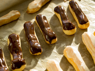 Freshly baked crispy oblong and round pastry chocolate eclairs and profiteroles on backing sheet
