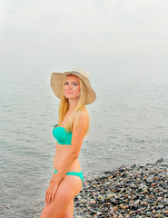 Beautiful young woman in bikini posing on a sea beach. Blonde Girl wearing in the green bikini and hat. Vacation on the sea