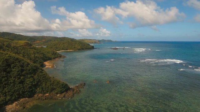 The coast of the tropical island with the mountains and the rainforest on a background of ocean with big waves.Aerial view: sea and the tropical island with rocks, beach and waves. Seascape: sky