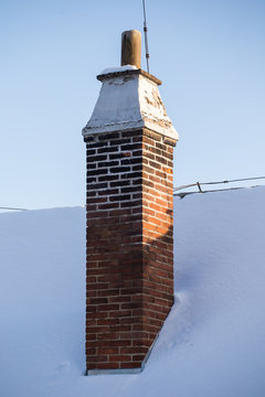 Old brick chimney and roof covered with snow