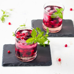 Cold cocktail with currants, blueberries, blackberries and ice cubes on black slate plates. White textured background. Square