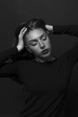 Black and white portrait of a sad girl dressed in black blouse. Devush with long curly hair. Gentle make-up and beautiful freckles.