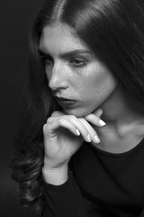 Black and white portrait of a sad girl dressed in black blouse. Devush with long curly hair. Gentle make-up and beautiful freckles.