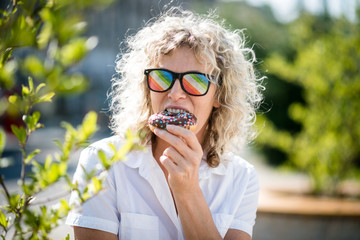 Woman wearing colorful goggles and enjoying doughnut