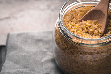 Grain bulgur in a glass jar and in a spoon close-up