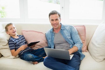 Father and son using laptop and digital tablet in living room