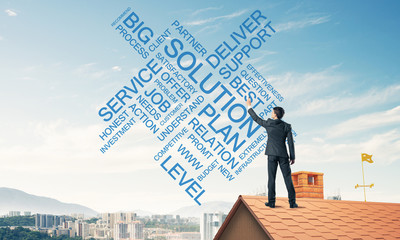 Young businessman standing on house roof and writing leadership 