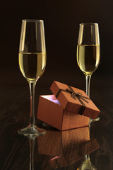 Two glasses with white wine and gift box on mirror table. Celebrities composition.