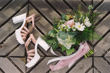 Botanic bridal chic. Top view of modern bride outfit. Bouquet with silk ribbons and platform shoes on wooden background.