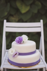 White wedding cake with purple decoration outdoors on white wooden chair