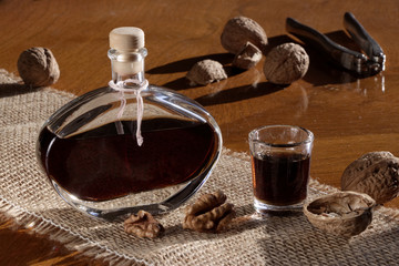 Walnut liqueur in a bottle and shot glass on a wooden table with scattered walnuts