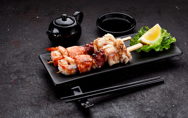 Tasty seafood skewers and soy sauce over dark concrete background