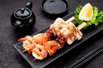 Tasty seafood skewers and soy sauce over dark concrete background
