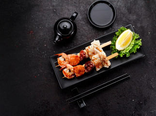 Tasty seafood skewers and soy sauce over dark concrete background