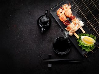 Tasty seafood skewers and soy sauce over dark concrete background