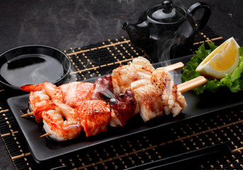 Tasty seafood skewers and soy sauce over dark concrete background