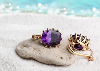 Gold Jewelry earrings with gems on sand beach background, soft f