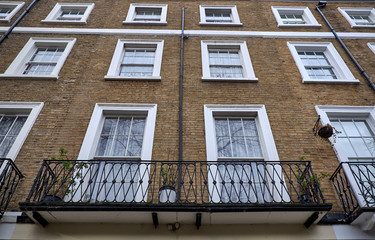 Obraz premium Brown brick facade with white decorations around rectangle shaped colonial style windows and balconies of a british apartment building in London City