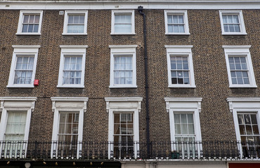 Fototapeta na wymiar Brown brick facade with white decorations around rectangle shaped colonial style windows of a british apartment building in London City
