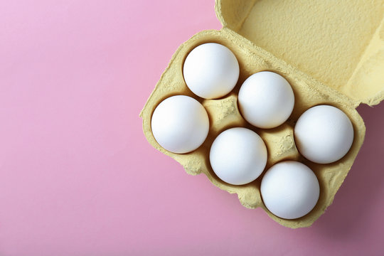 Raw eggs in package on pink background