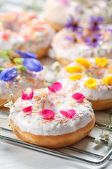 Delicious donuts and flowers on baking rack and white background, closeup