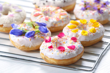 Delicious donuts and flowers on baking rack and white background, closeup