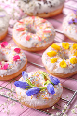 Delicious donuts and flowers on baking rack and wooden table, closeup