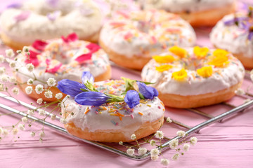 Delicious donuts and flowers on baking rack and wooden table, closeup
