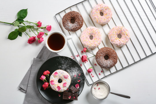 Delicious donuts, flowers and cup of coffee on white table