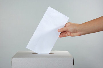 Female hand putting voting ballot into the box  on color background