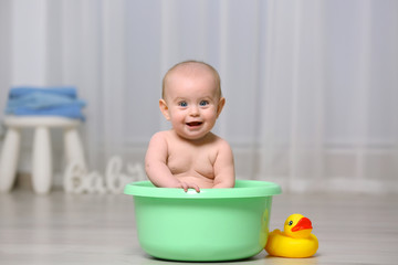 Cute baby in plastic basin at home