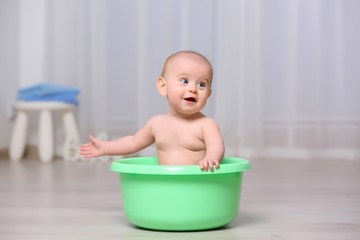 Cute baby in plastic basin at home