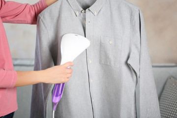 Woman ironing shirt with garment steamer - obrazy, fototapety, plakaty