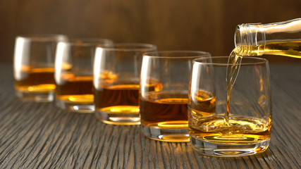 Pouring whiskey into the glass on a wooden table