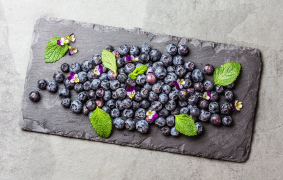 Berry fresh blueberries with mint leaves on black slate board