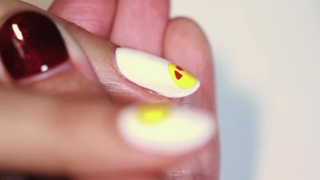Manicure procedure woman hand drawing yellow emoji on white finger nail polish, close up