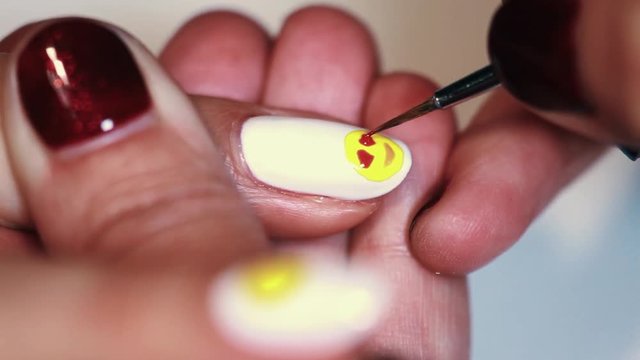 Manicure procedure woman hand drawing yellow emoji on white finger nail varnish, close up