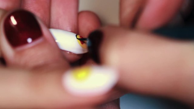 Manicure procedure woman hand painting yellow emoji on white finger nail polish, close up
