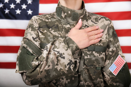 Close up view of female soldier holding hand on heart, with USA flag on background