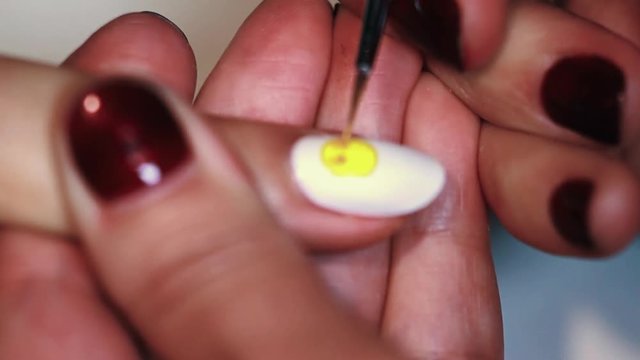 Manicure procedure female hand draws yellow emoticonon white finger nail polish, close up