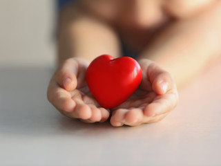 Child holding small red heart, closeup. Adoption concept