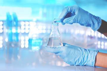 Hands in gloves pouring sample into flask, closeup