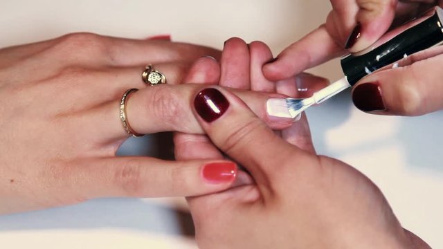 Woman cosmetician hand brushing plain white polish on nails in beauty saloon, close up